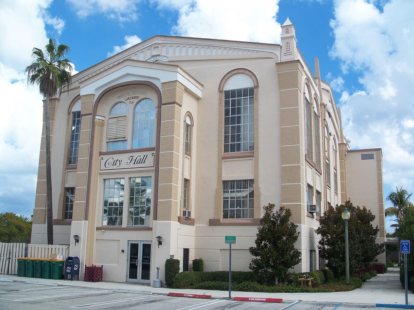 Cream stucco city hall building with arched windows and a palm tree under a blue sky.