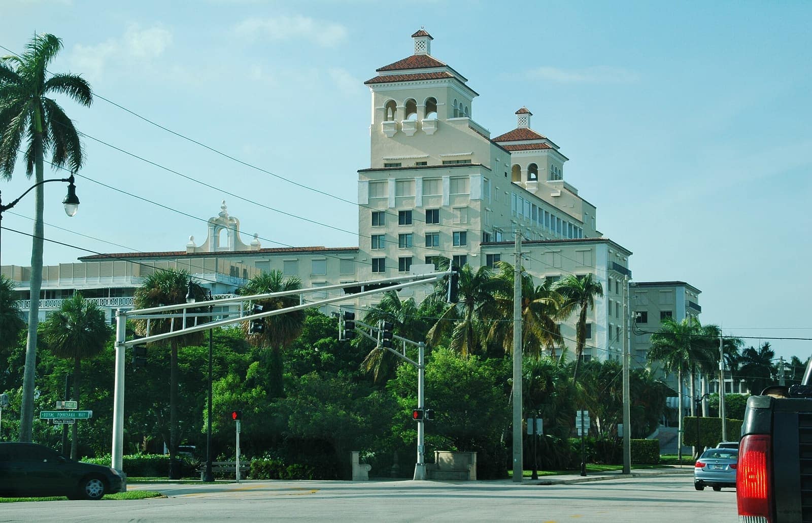 Large cream-coloured hotel building behind palm trees and traffic signals at a street crossing.