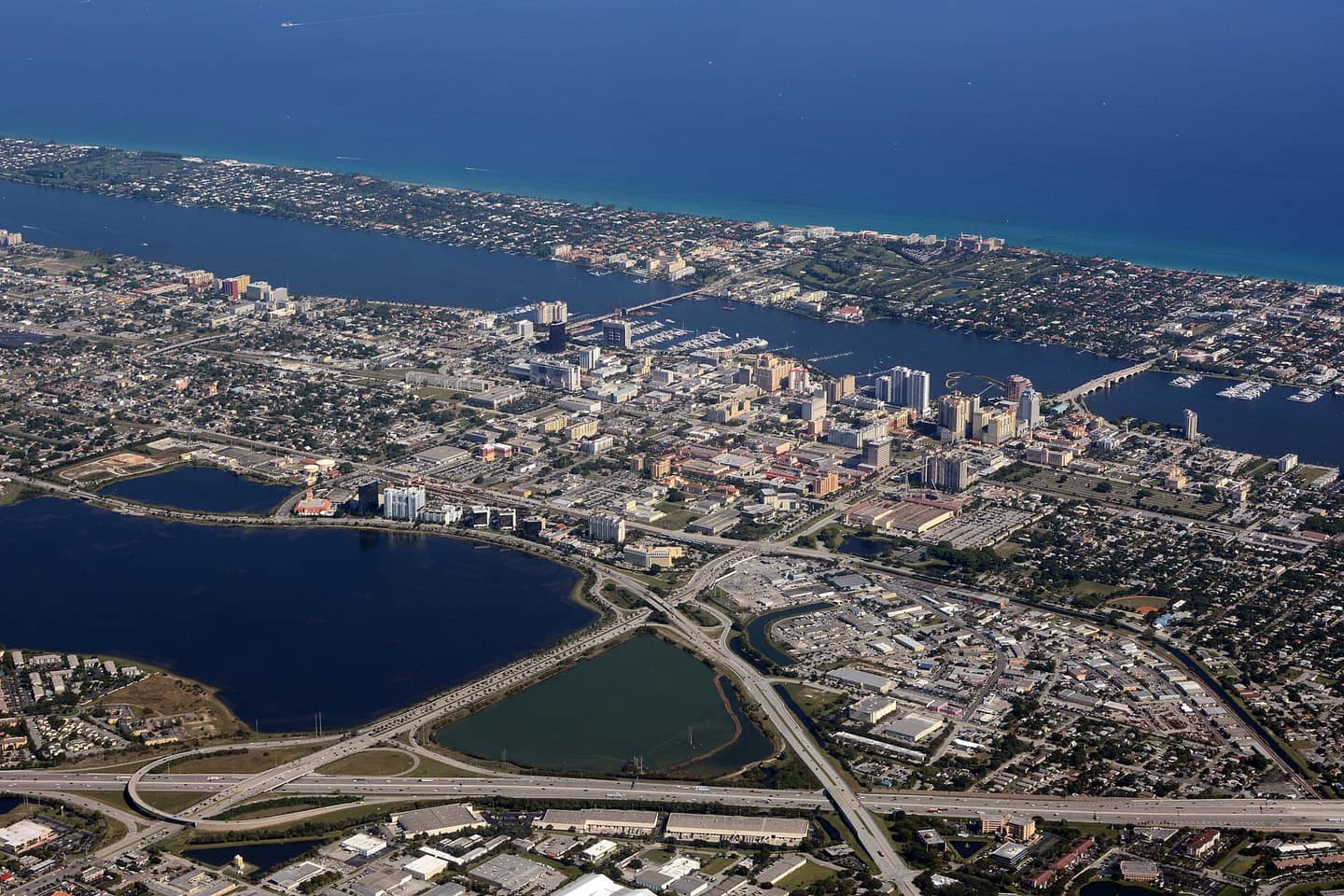 Aerial view of a coastal city with a waterway, causeway bridges, and highways under clear blue sky.