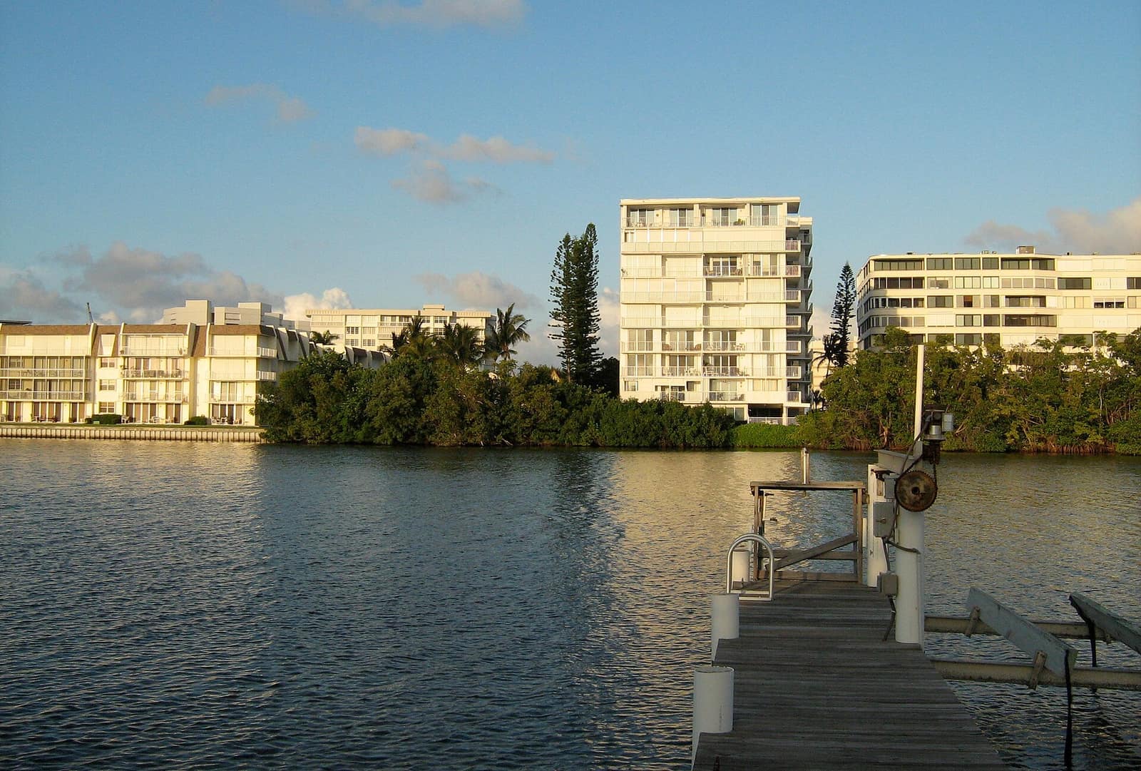 Waterfront condominium towers across calm water from a wooden dock in warm evening light.