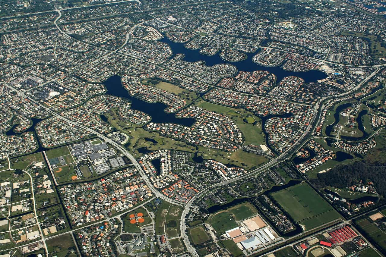 Aerial view of dense suburban housing developments with lakes, roads and green fields.
