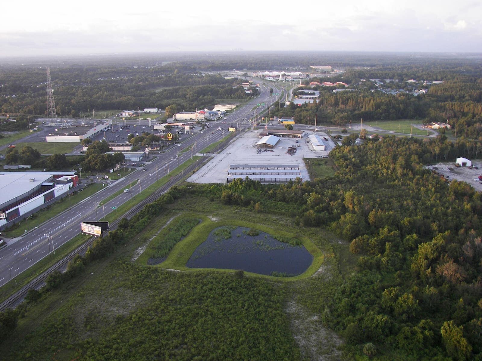 Aerial view of a wide highway lined with commercial buildings, parking lots, and a retention pond.
