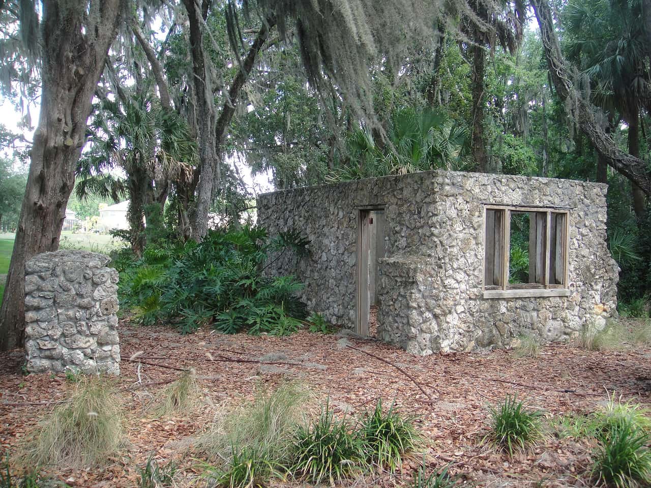 Weathered stone ruin with a doorway and window opening, surrounded by live oaks draped in Spanish moss.