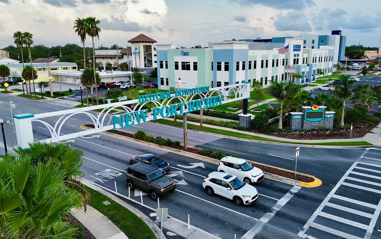Drone view of an arched New Port Richey sign spanning a multi-lane road with cars and modern buildings.