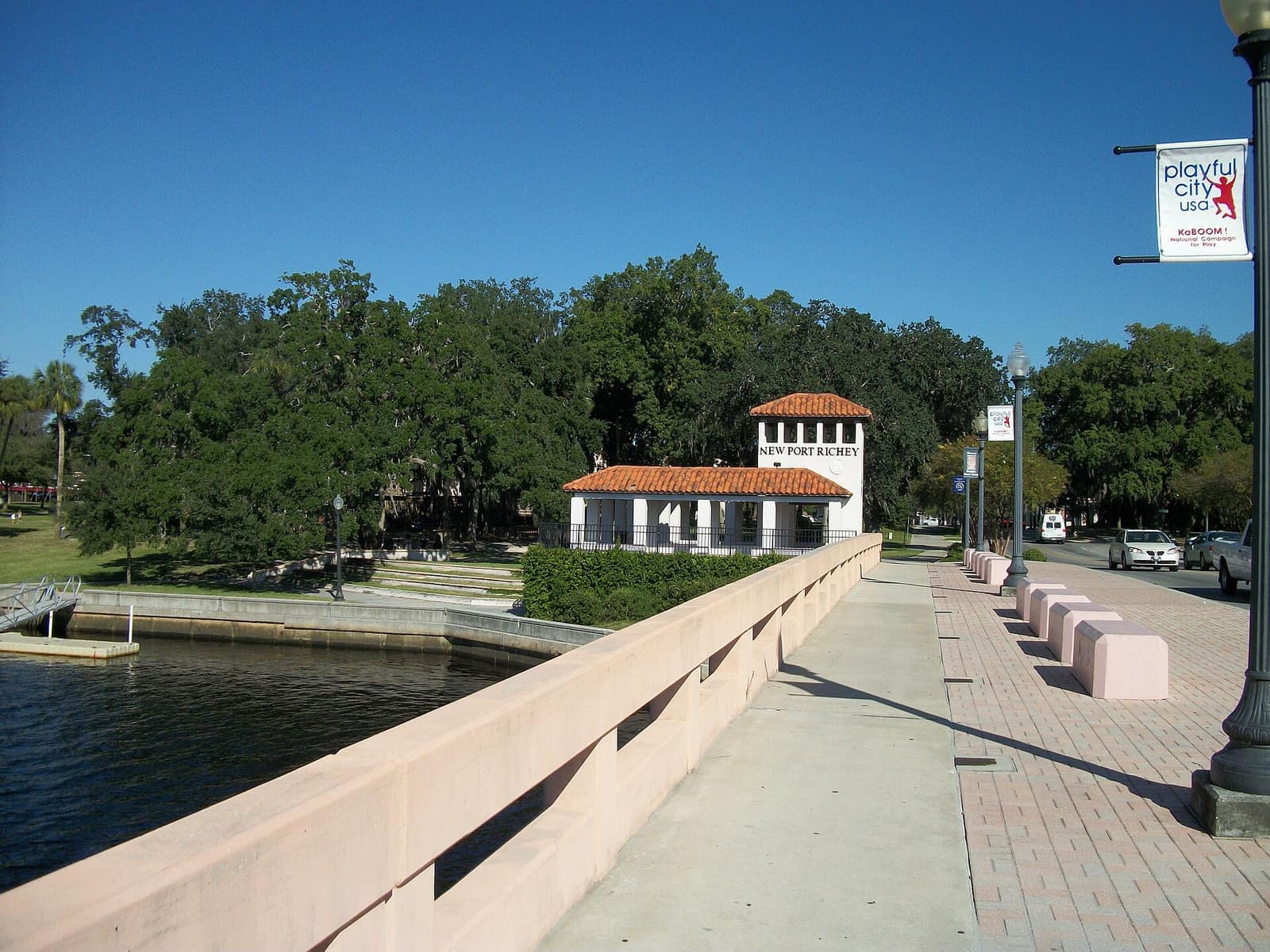 Pink-railed riverside walkway leading to a white domed-roof tower with a red tile roof beside a river.