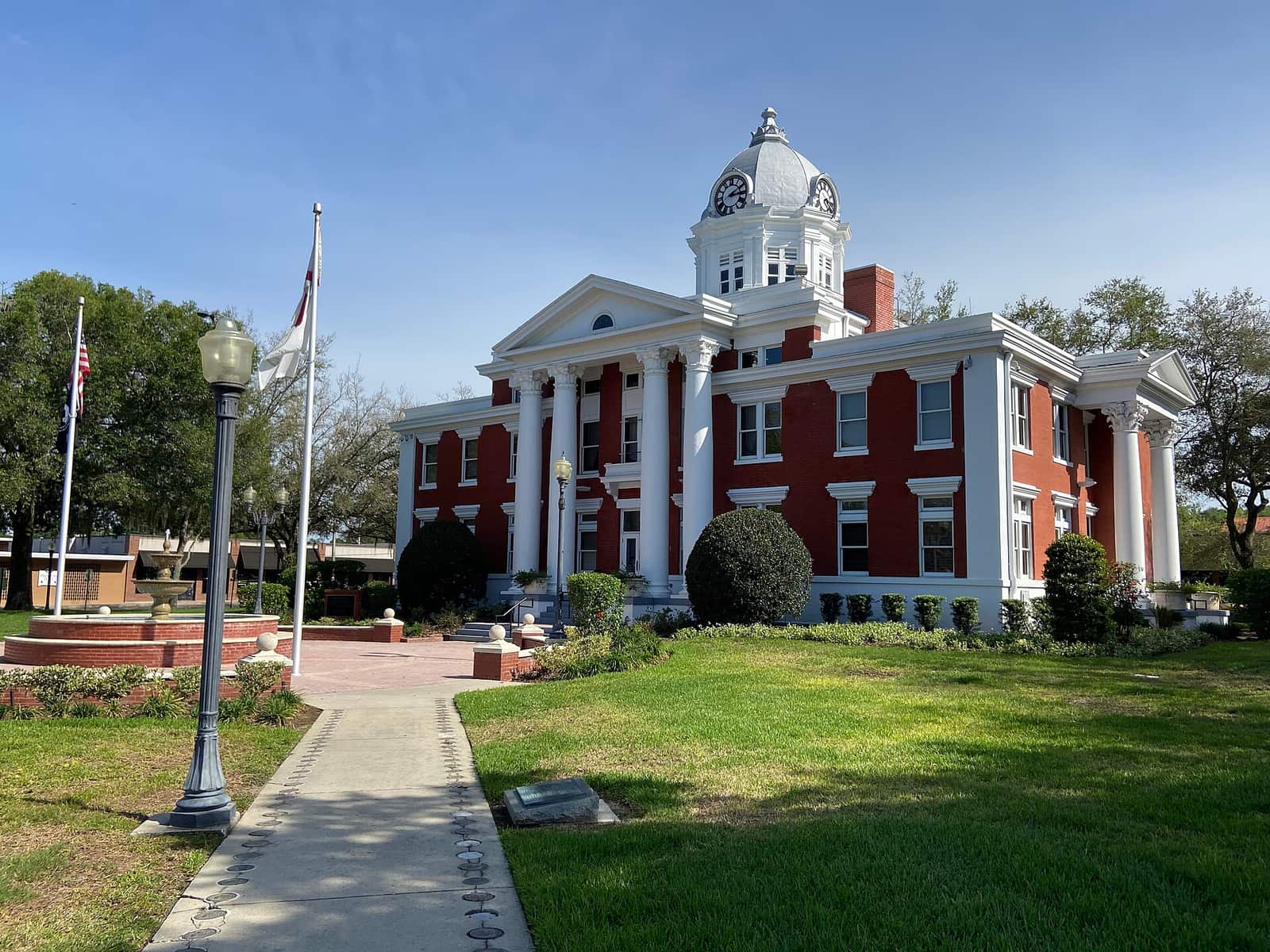 Red brick courthouse with white columns and domed clock tower under blue sky with lawn.