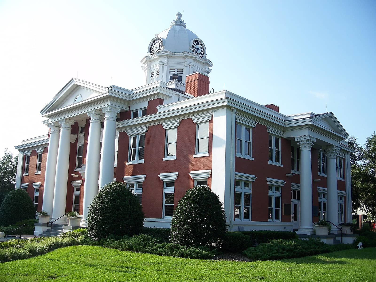 Red brick courthouse with white columns and a domed clock tower under a clear blue sky.