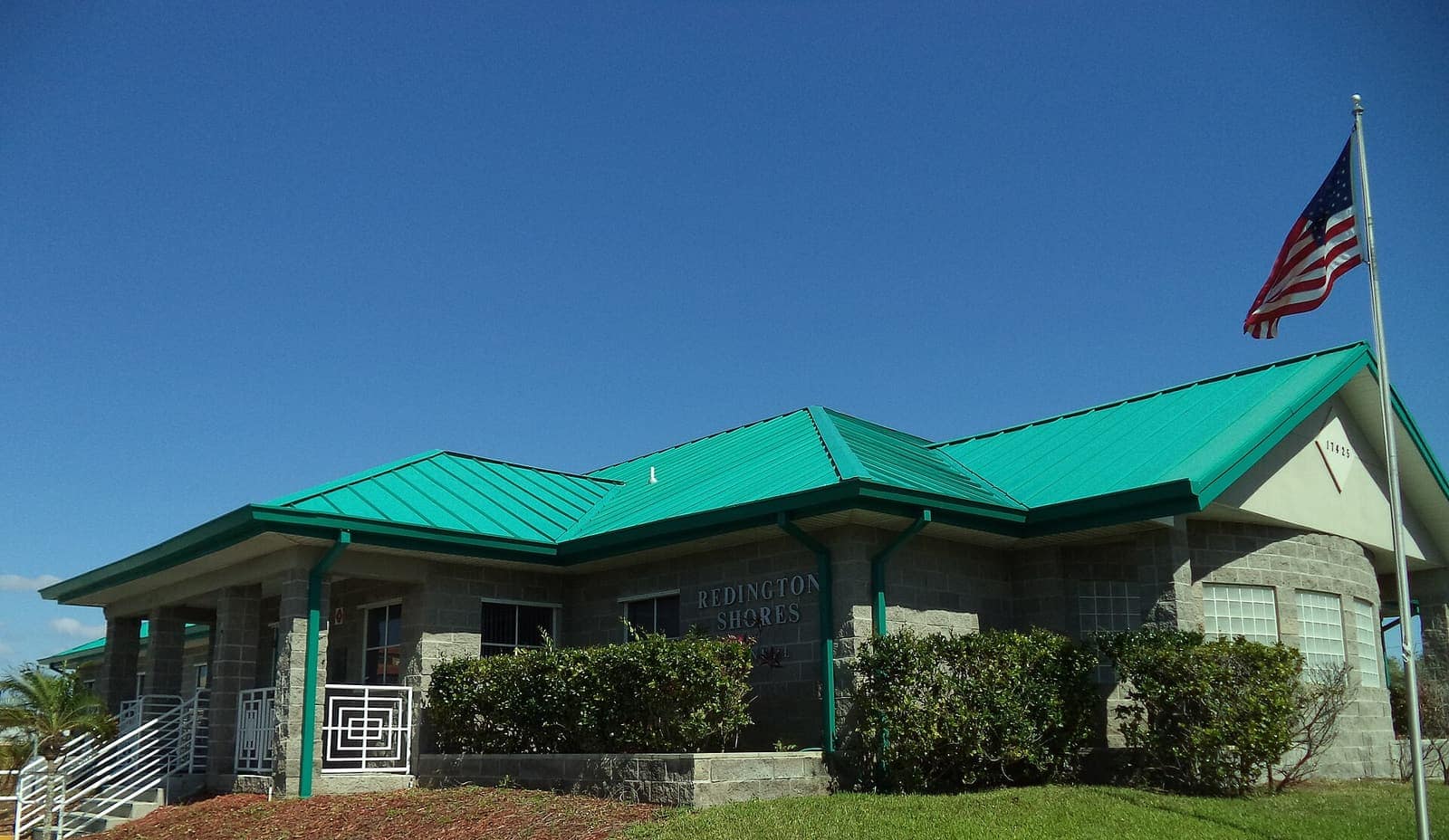 Single-storey brick building with a green metal roof and an American flag on a pole.
