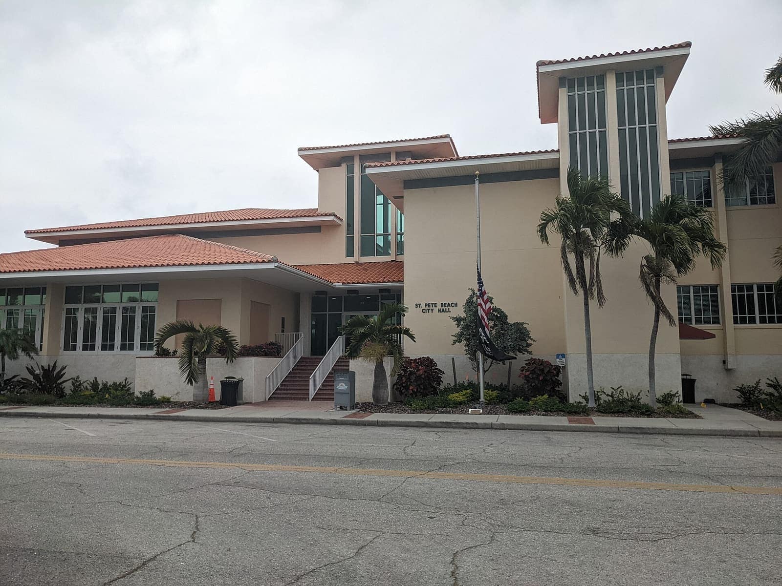 Two-story cream municipal building with terracotta roof, palm trees, and a flag in front.