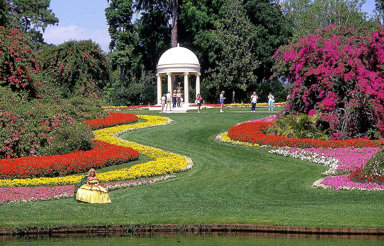 Formal gardens with a white domed gazebo, colorful flower beds, and a few distant visitors on a green lawn.