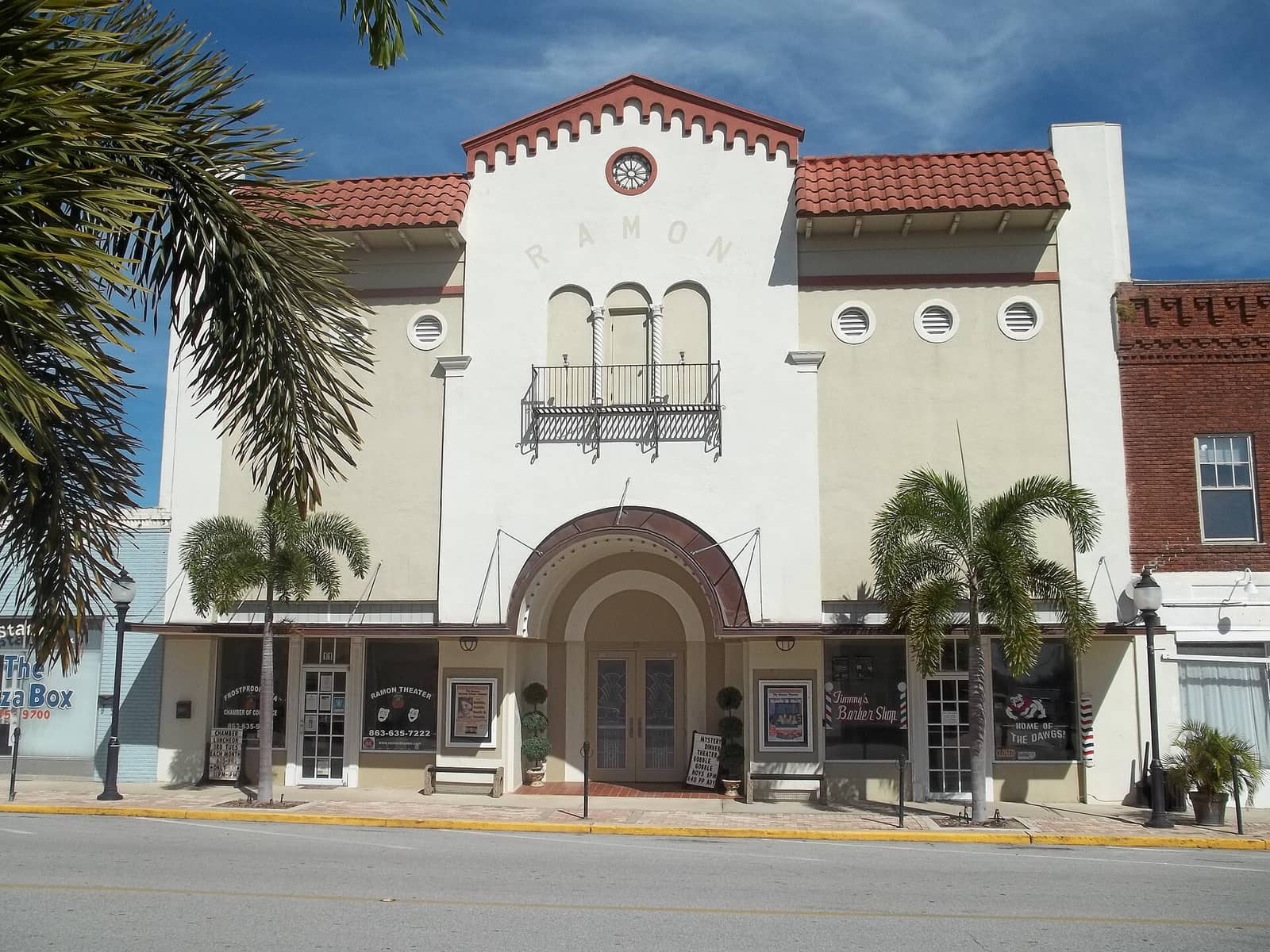 Cream stucco Ramon Theater facade with red tile roof, arched entrance and palm trees along the street.