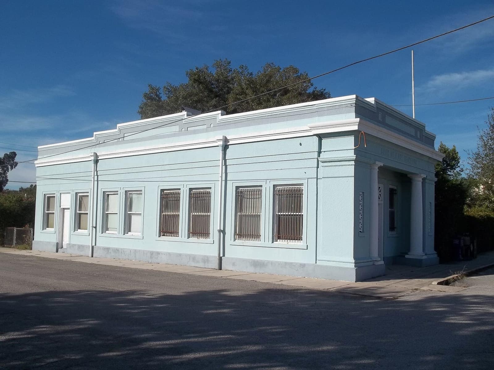 Long pale blue bank building with tall windows and columns under a clear blue sky.