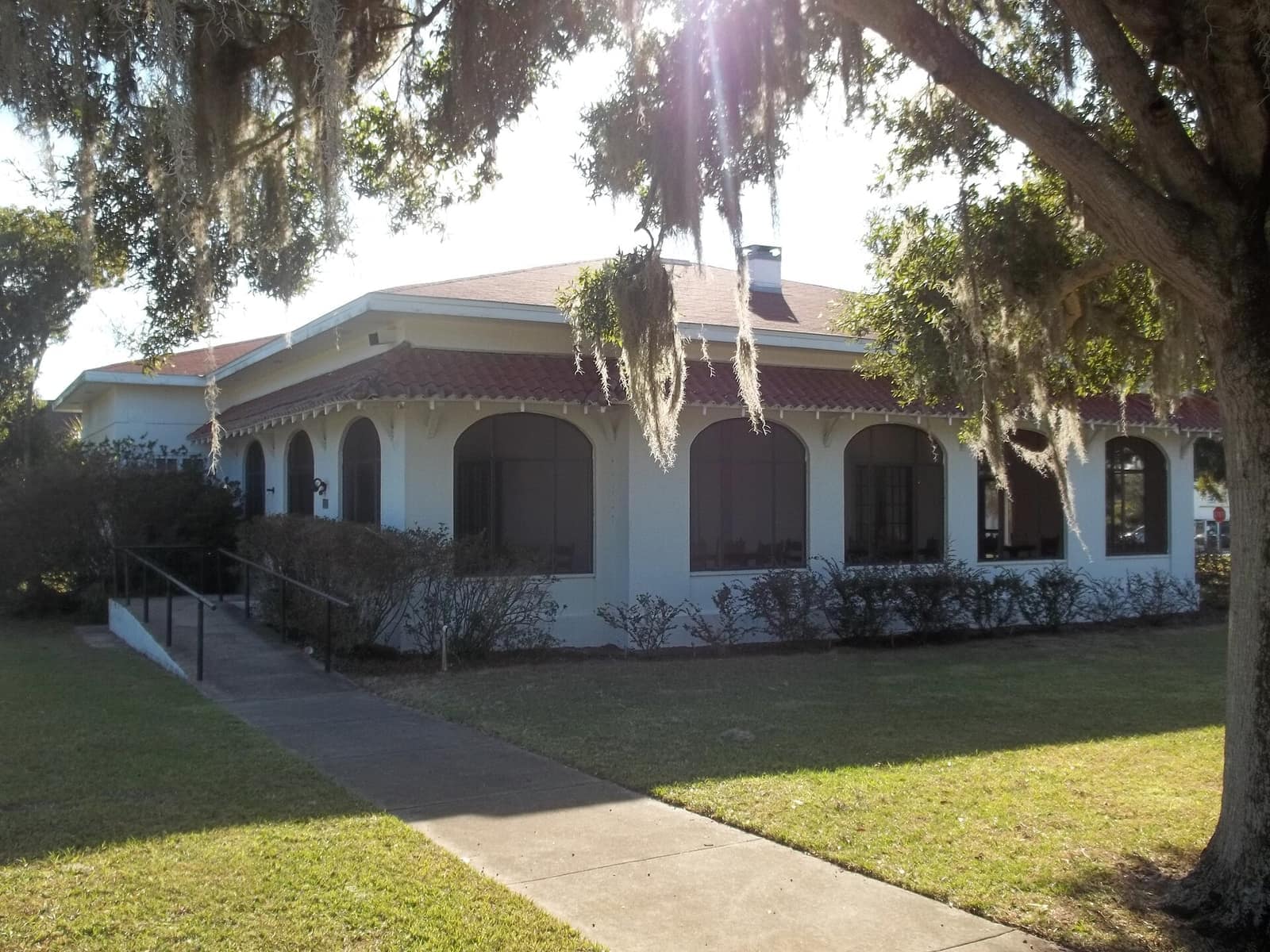 Cream stucco clubhouse with arched windows and a red tile roof, with Spanish moss hanging from a tree.