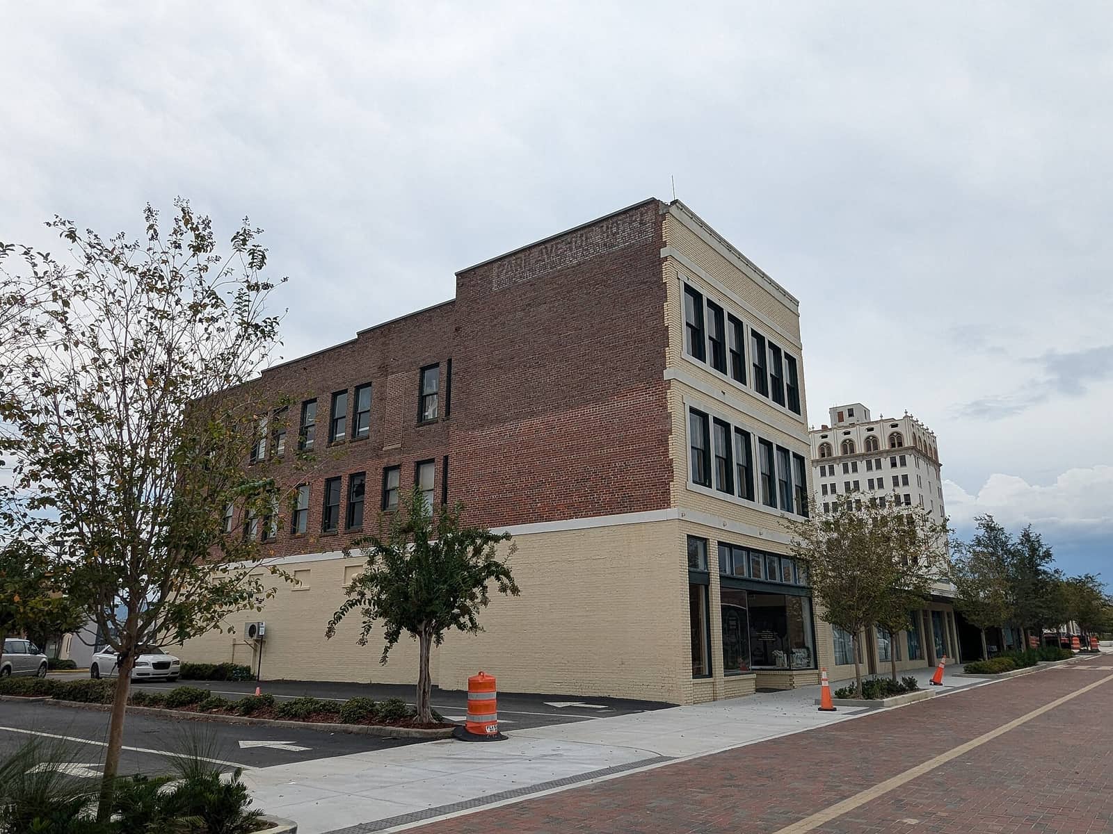 Three-story brick and cream commercial building on a downtown corner beside a red brick sidewalk under overcast sky.