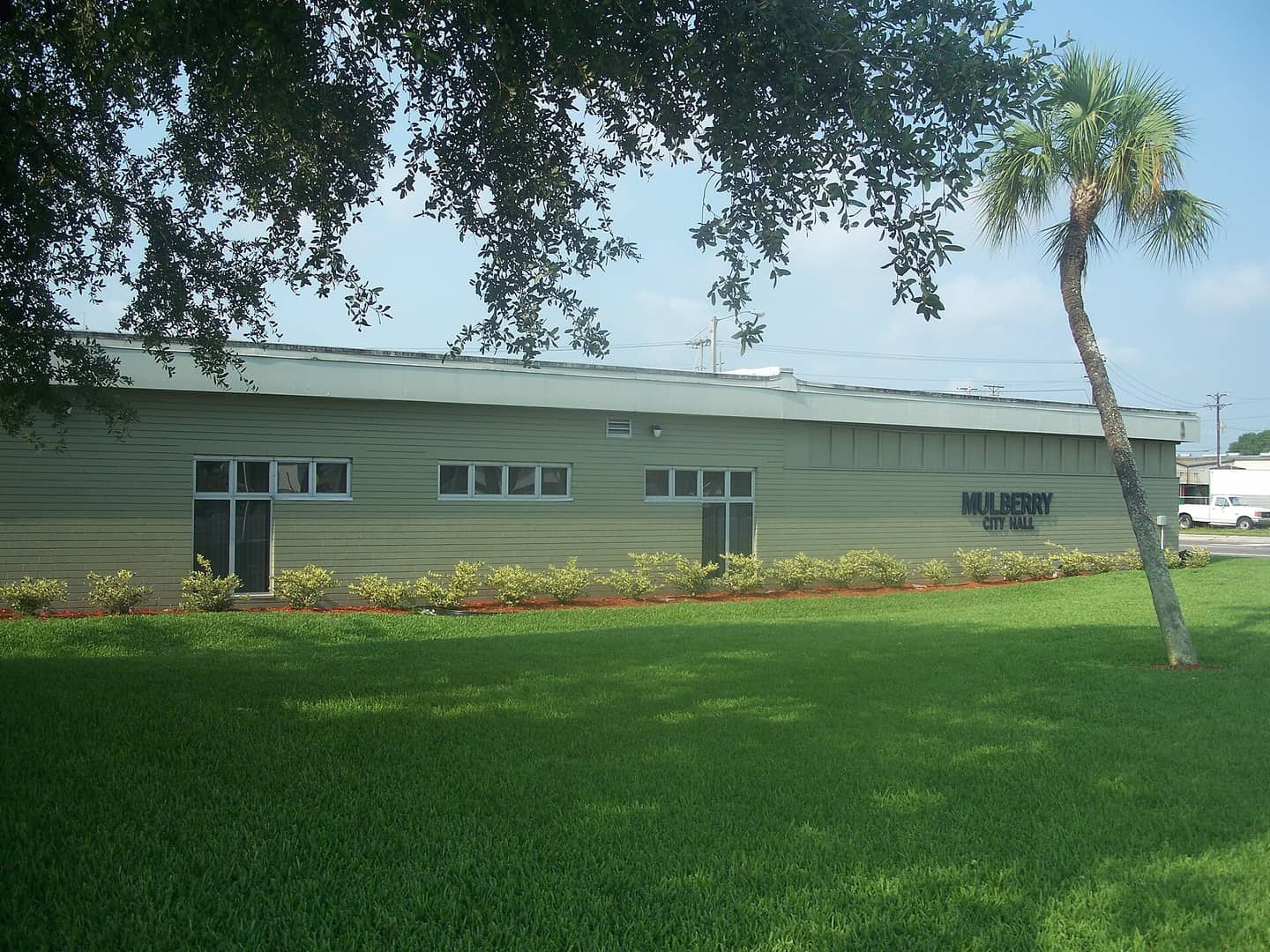 Long green-sided government building with a Mulberry City Hall sign, a palm tree and a large lawn.