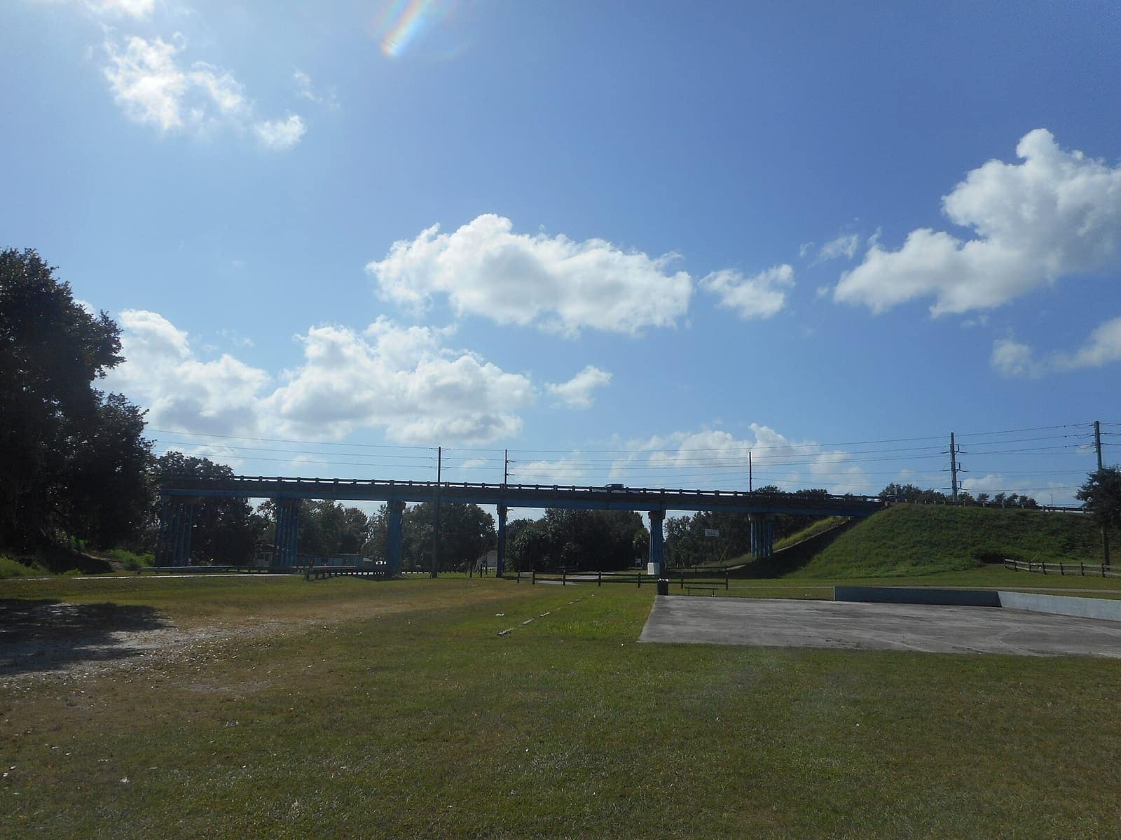 Blue highway bridge crosses over a grassy area under a partly cloudy sky.