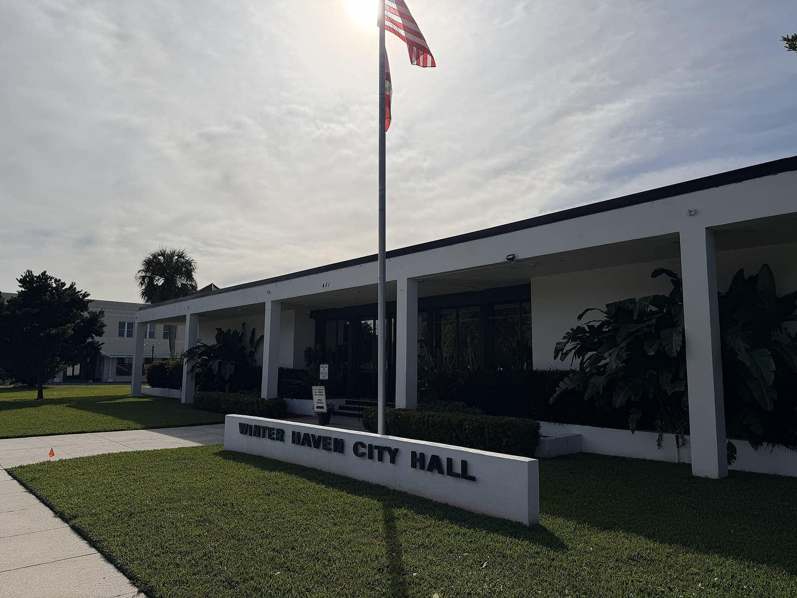 White single-story city hall building with a flagpole and a Winter Haven City Hall sign on the lawn.