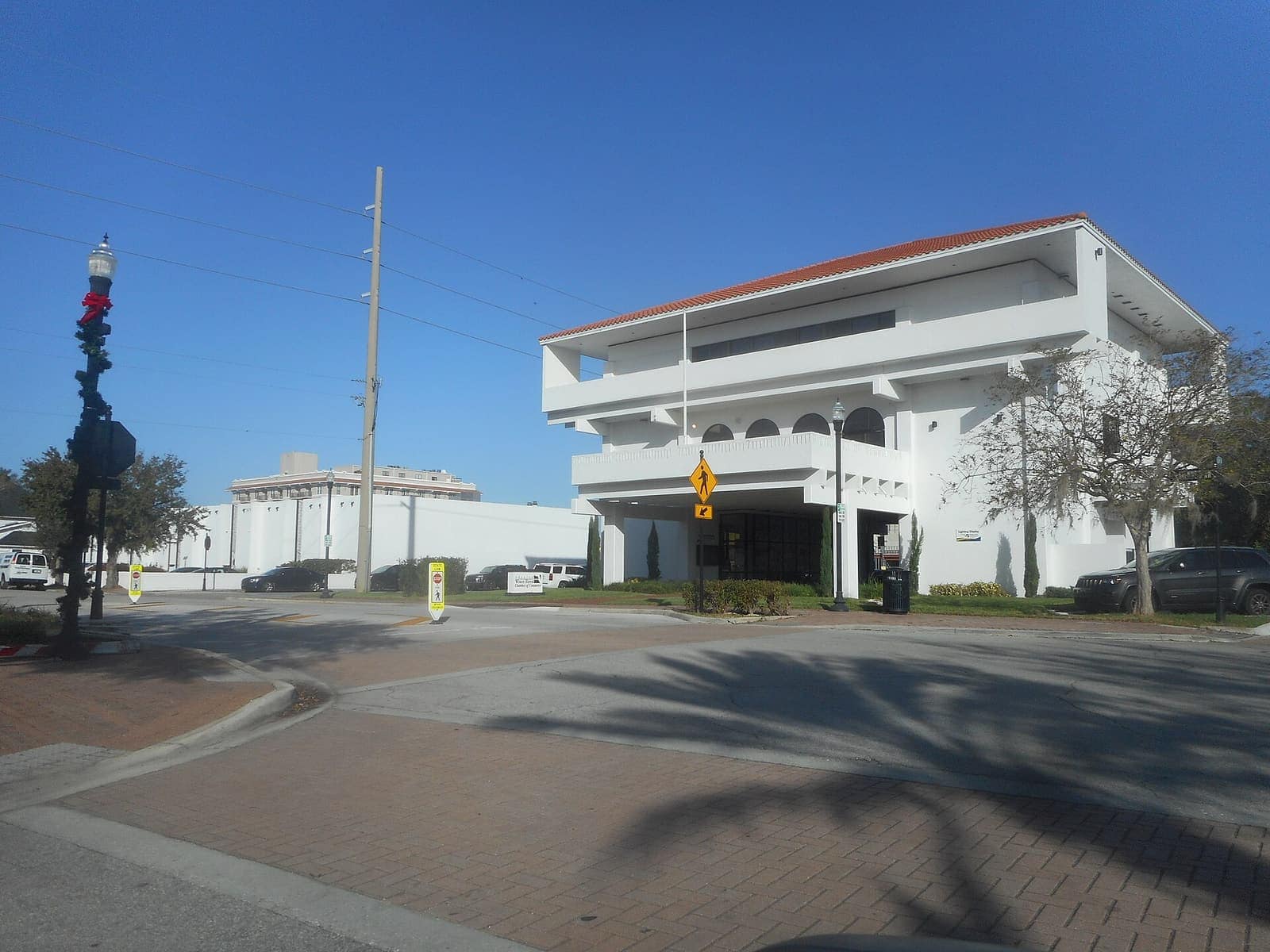Two-storey white modern building with a balcony and brick plaza at a sunny street corner.