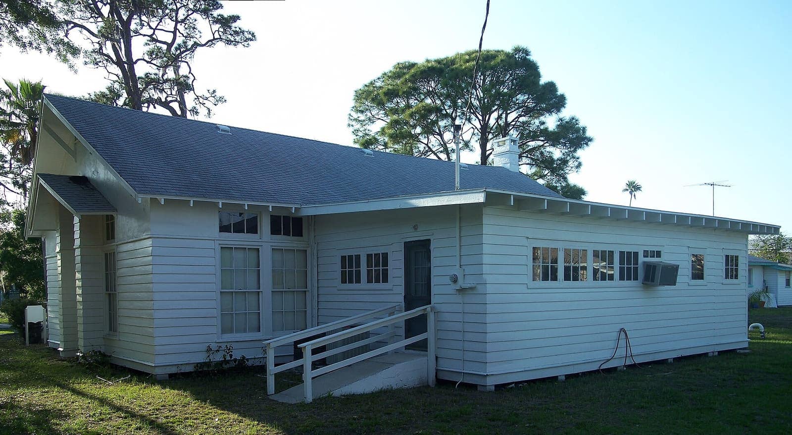 White wooden clubhouse with gabled roof and ramp beneath tall pine trees.