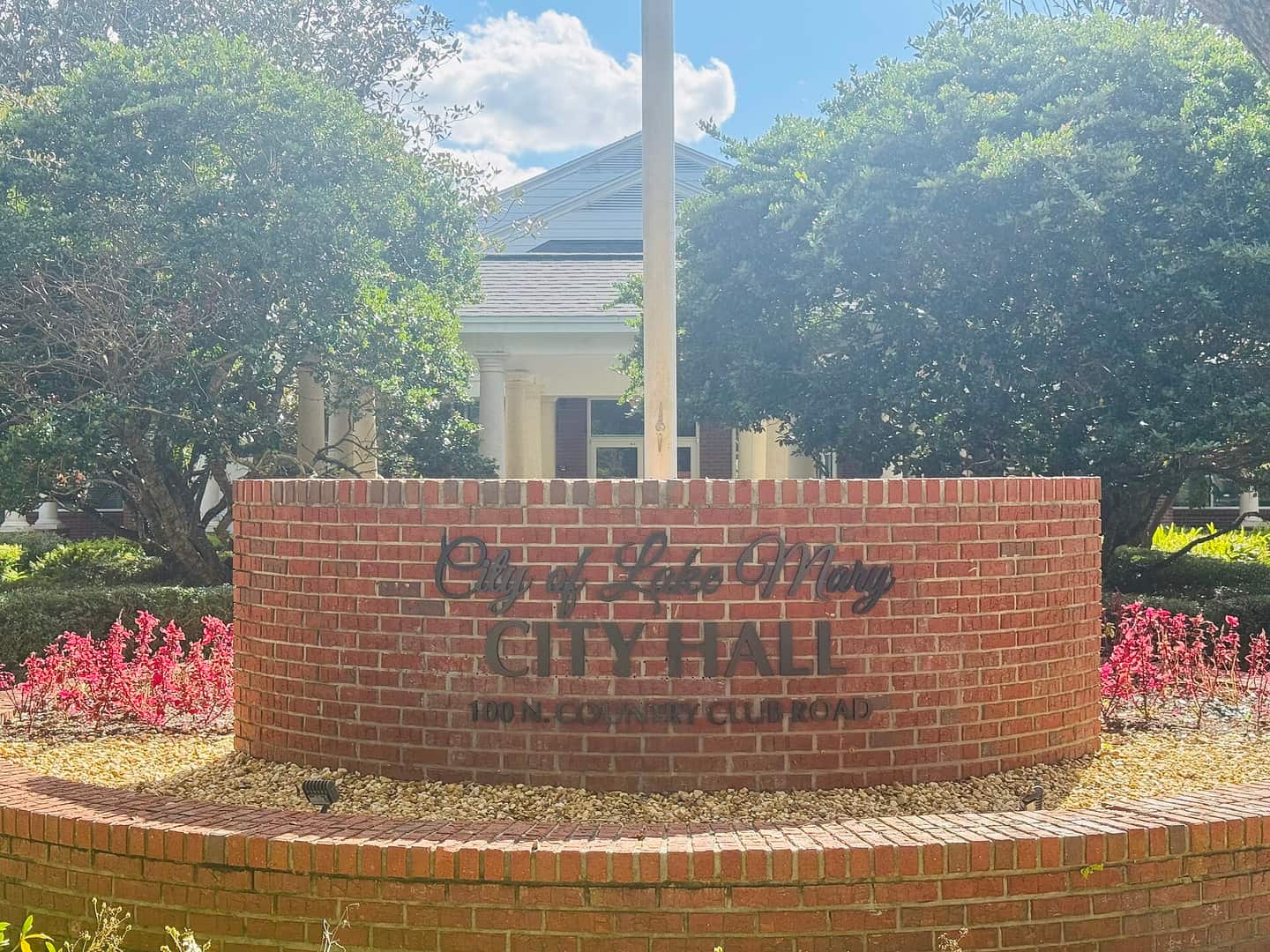 Curved brick monument sign reading City of Lake Mary City Hall, with a flagpole and building behind it.