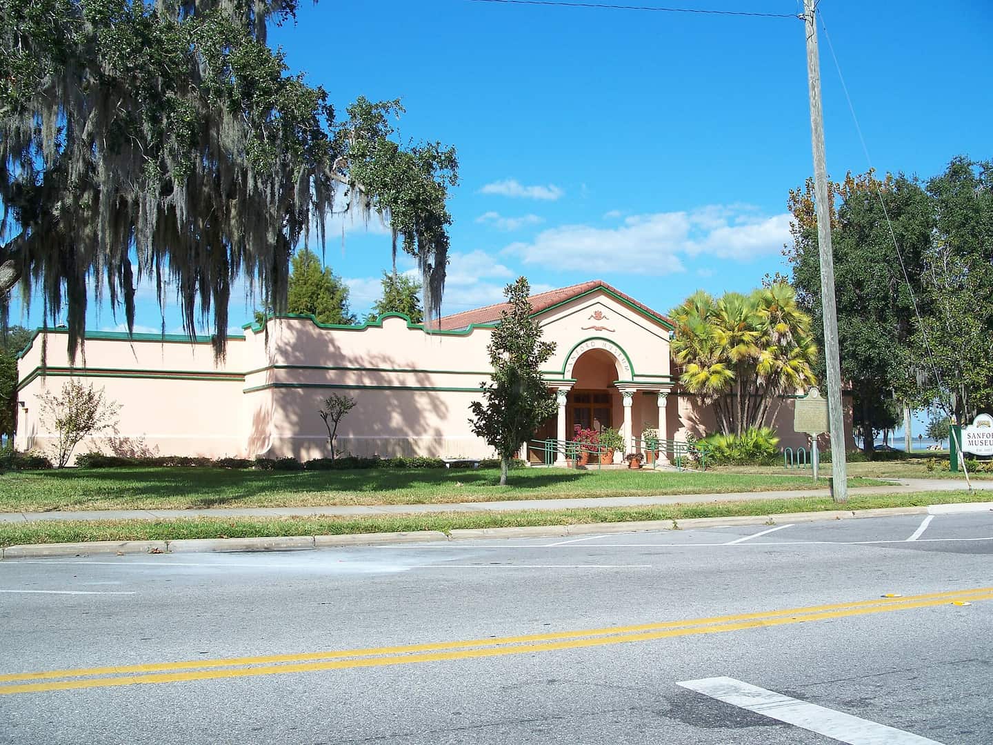 Pink stucco museum building with an arched entrance, Spanish moss trees and blue sky.