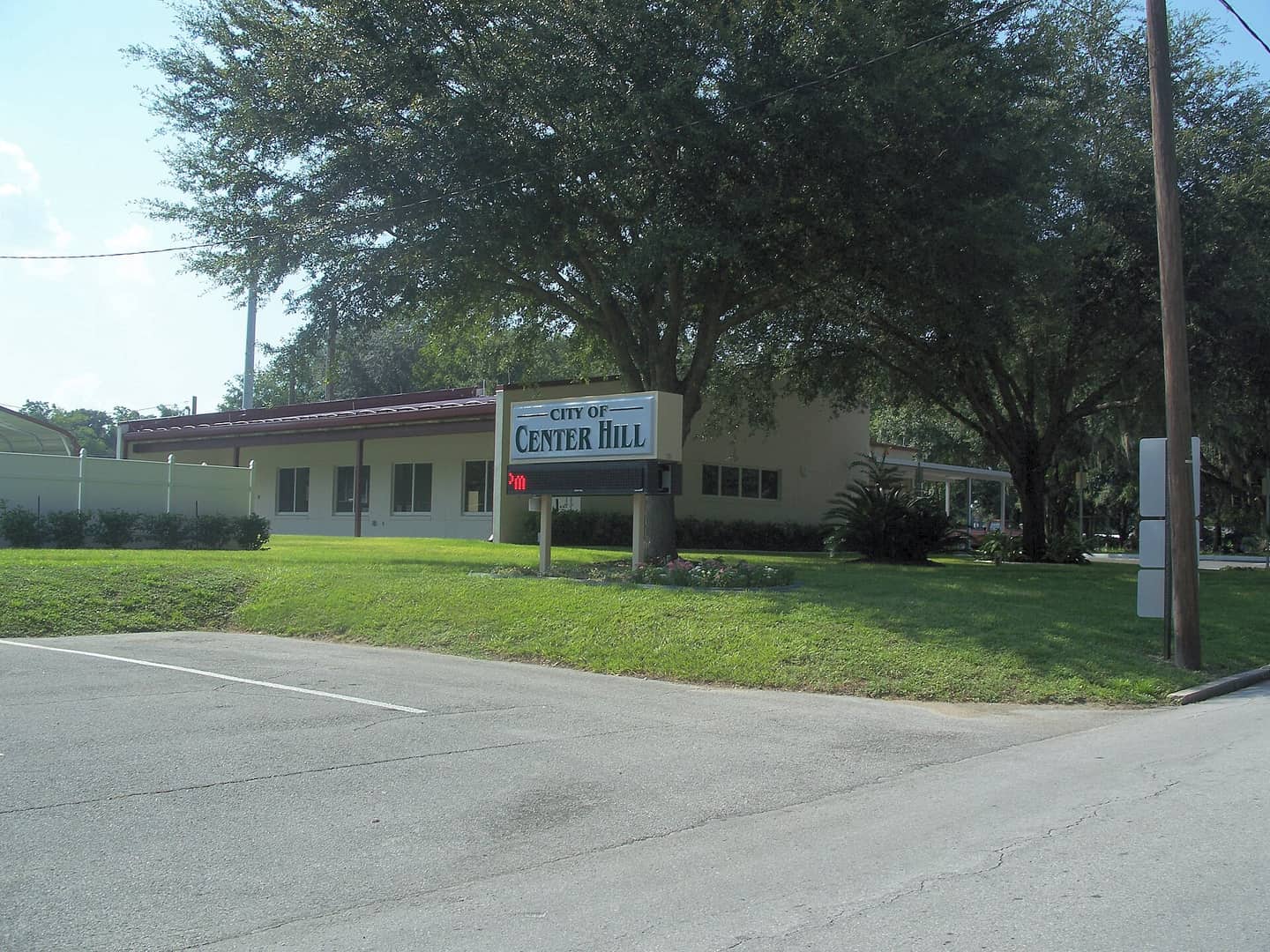 Single-story tan municipal building with a City of Center Hill sign and large oak trees.