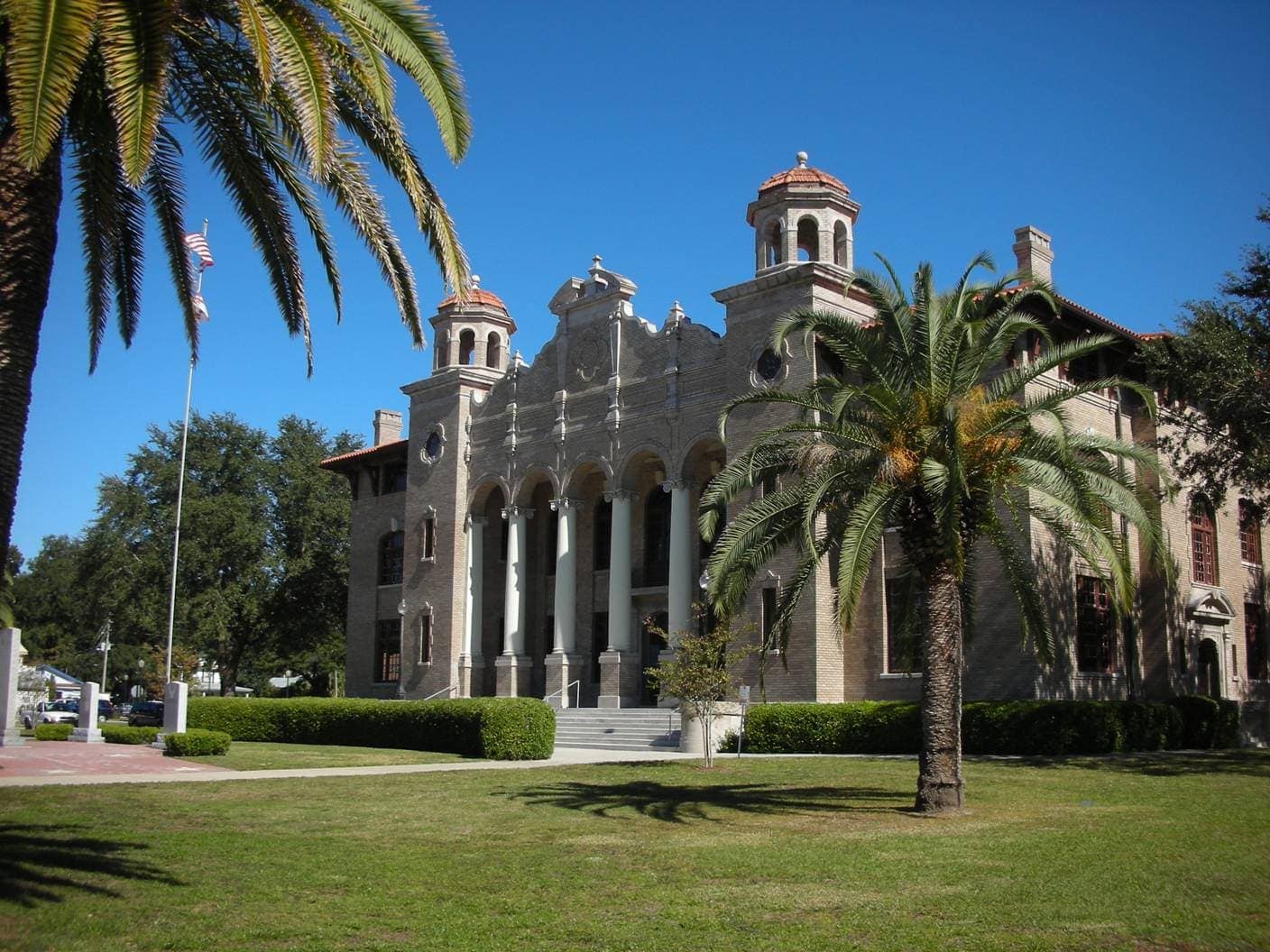 Historic brick courthouse with arched columns, domed towers, and palm trees under a clear blue sky.