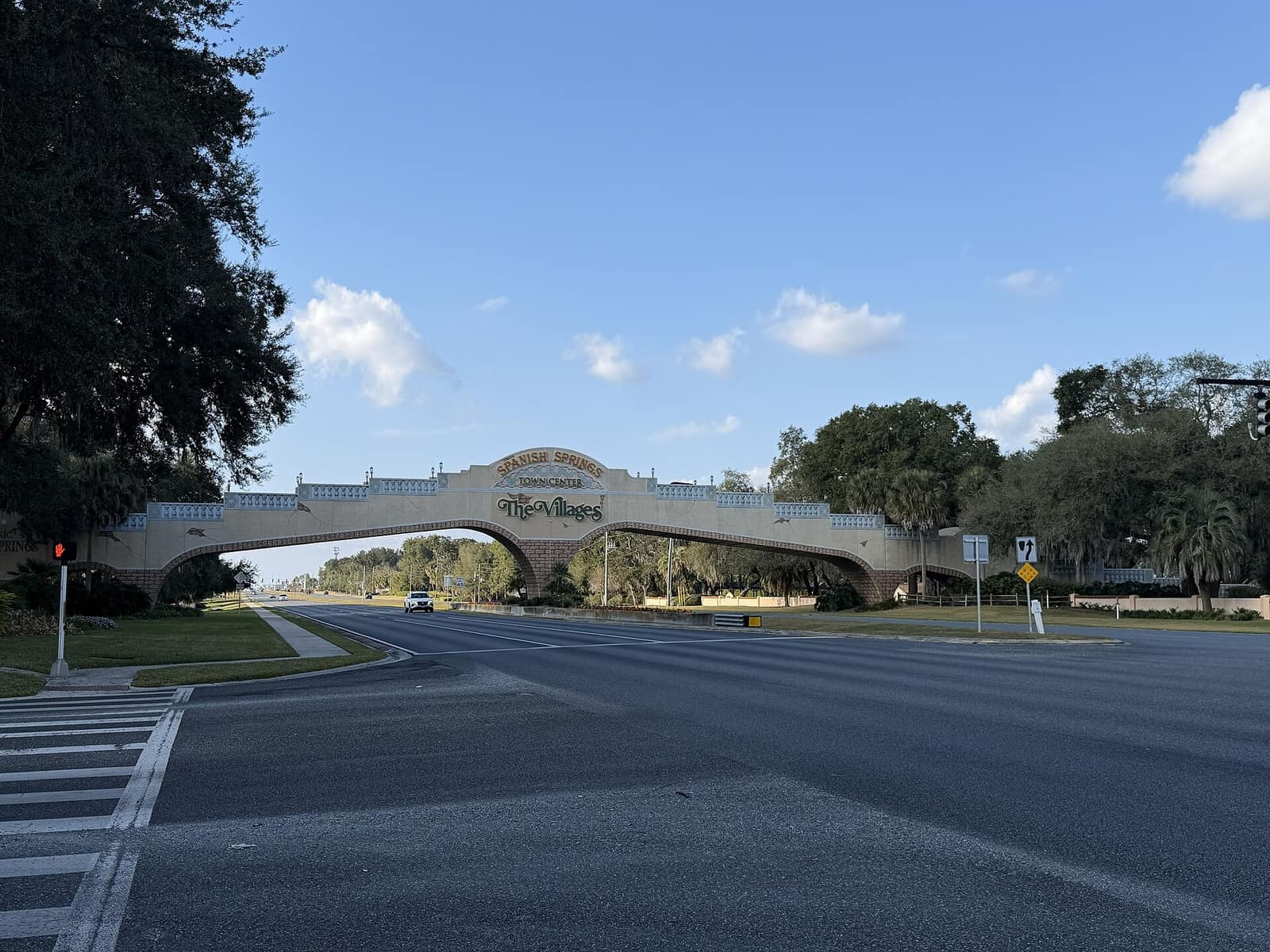 Stone arch entrance bridge spanning a multi-lane road under a clear blue sky, with a The Villages sign.